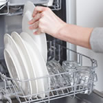 someone loading a white plate into a dishwasher with other plates and glasses