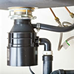 black garabage disposal under sink while hooked up to the bottom of the sink with pipes
