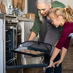 adult female and young female placing a sheet of cookies into an oven in the kitchen