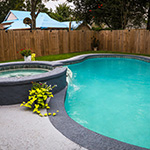 in ground pool with gray edging and hot tube and wood fence in the backyard