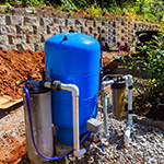 blue well pump with pipes and retaining wall and rocks